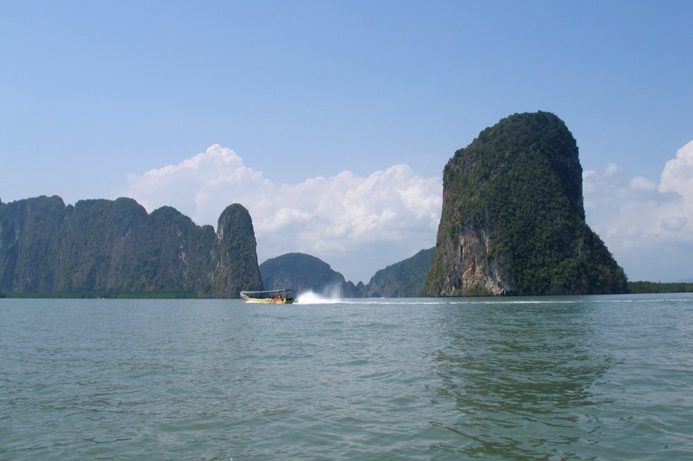 A longtail boat speeding past limestone cliffs in Phang Nga Bay